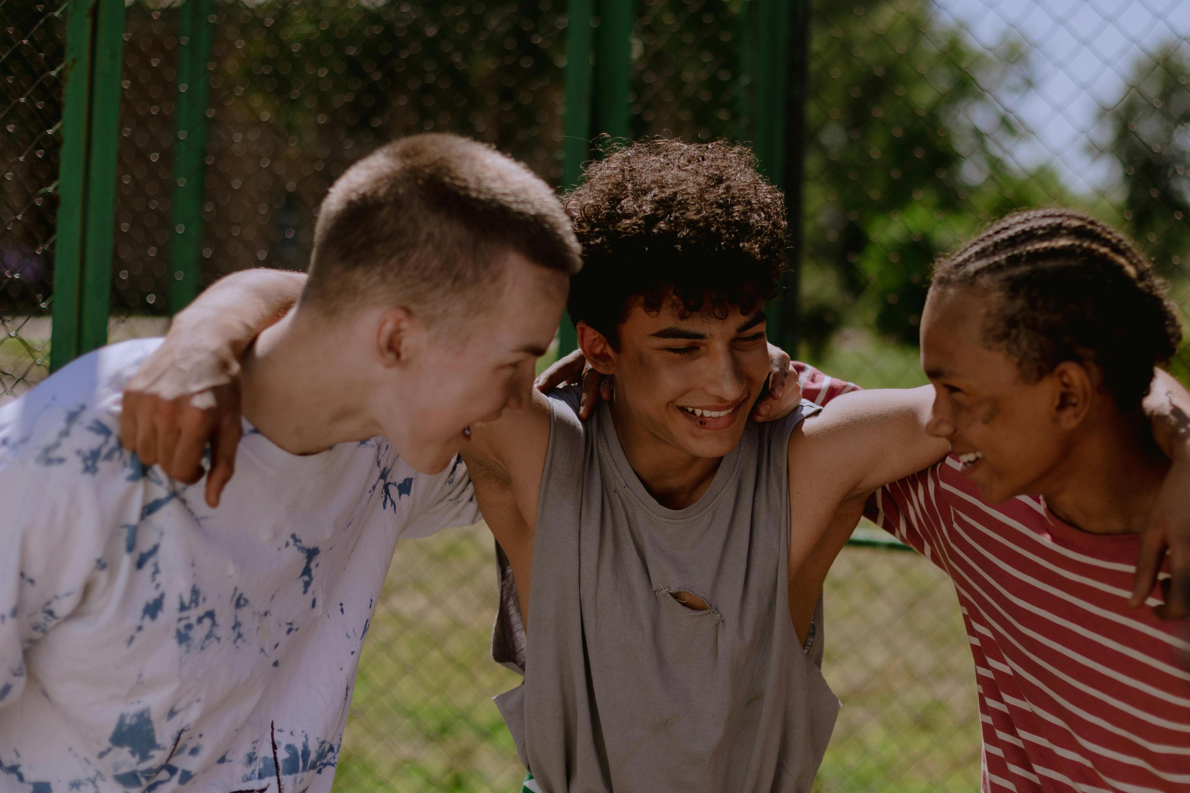 Three young people leaning on each other in laughter, arms around each other's shoulders.