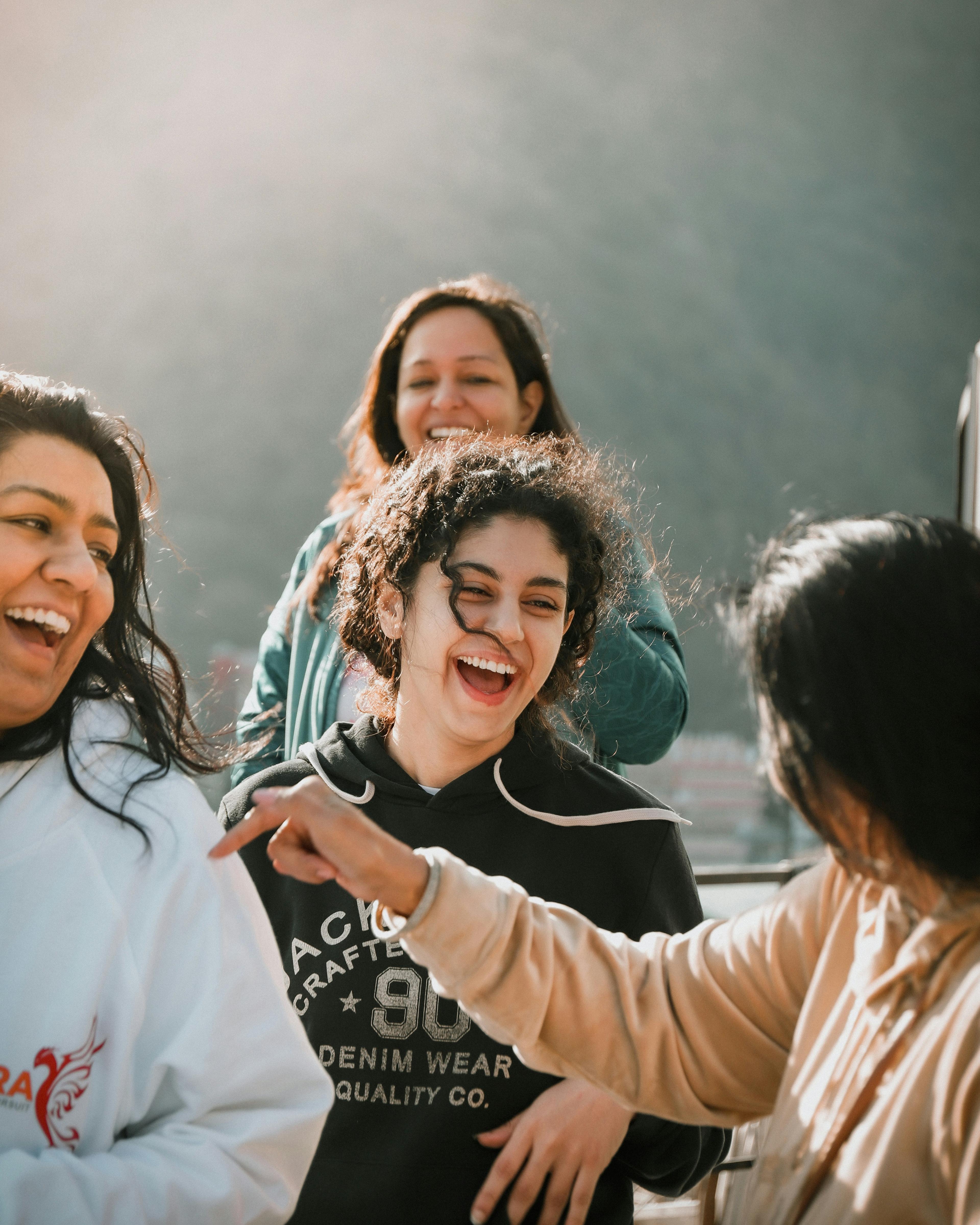 A small group of young people laughing together in soft outdoor light, leaning in mid-conversation.