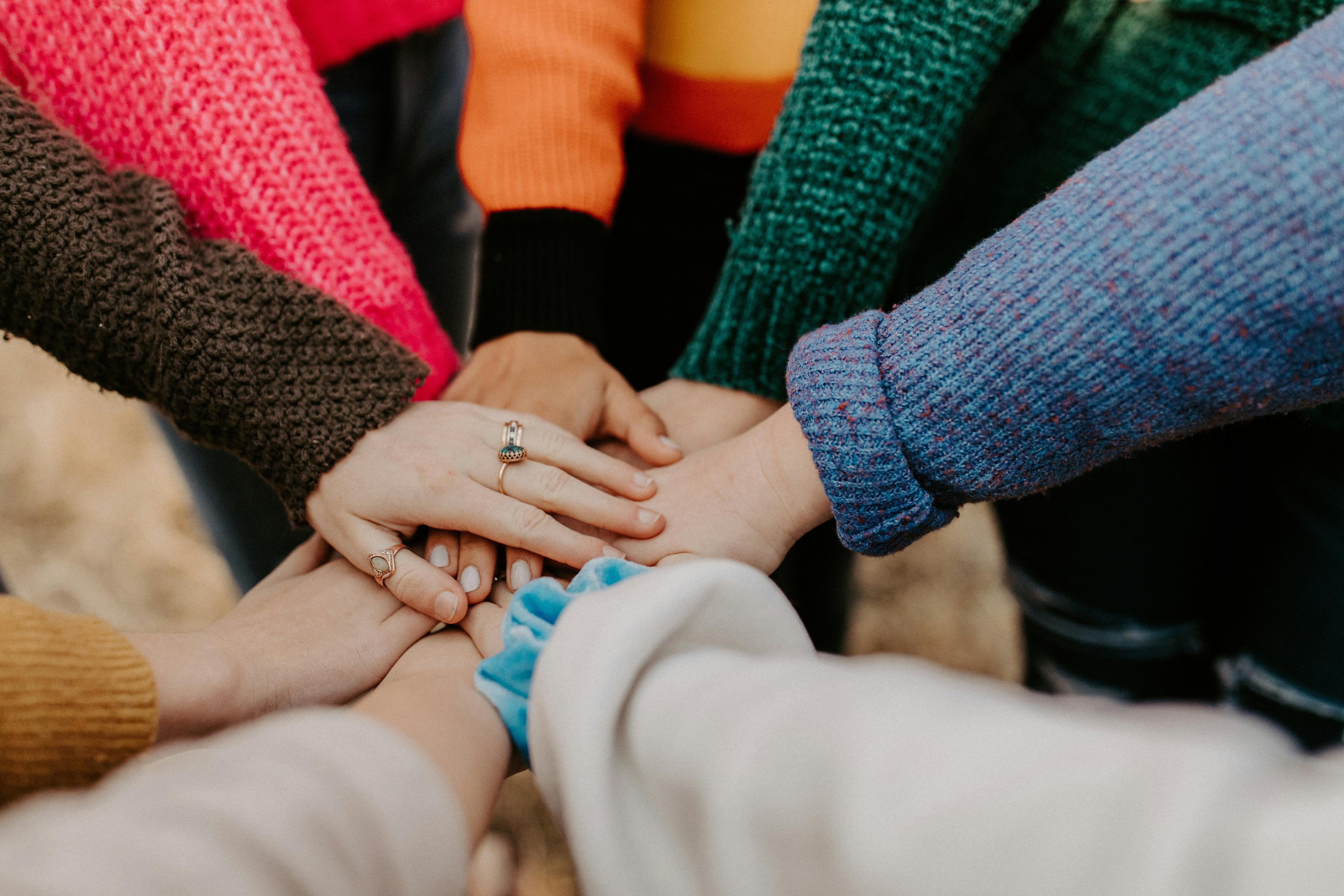 A circle of hands stacked together, layered in colourful sweater sleeves.