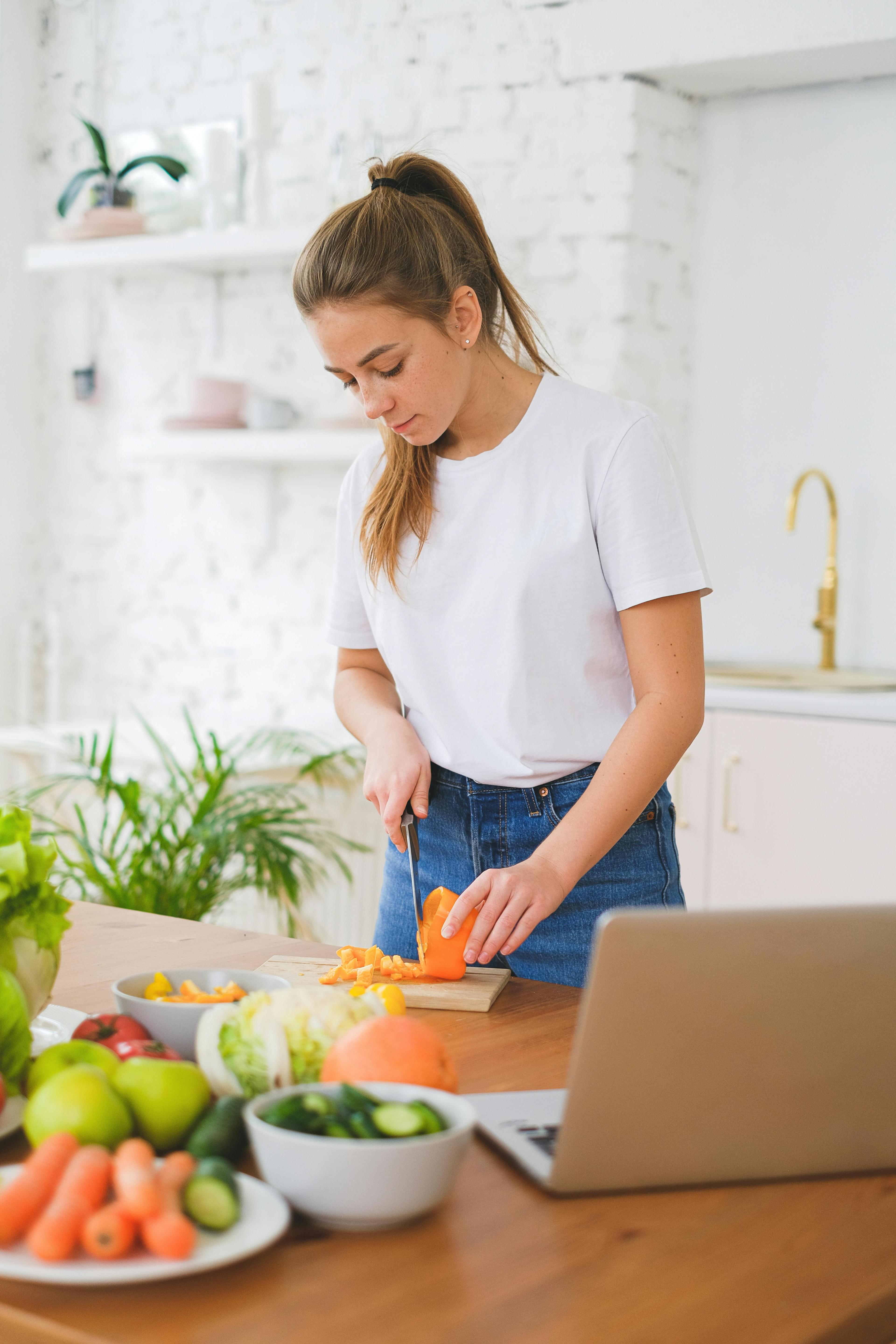 A young person preparing a meal in a bright kitchen, chopping vegetables at the counter.